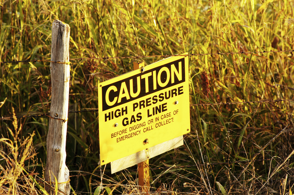 Sign next to a fence post with text - Caution High Pressure Gas Line
