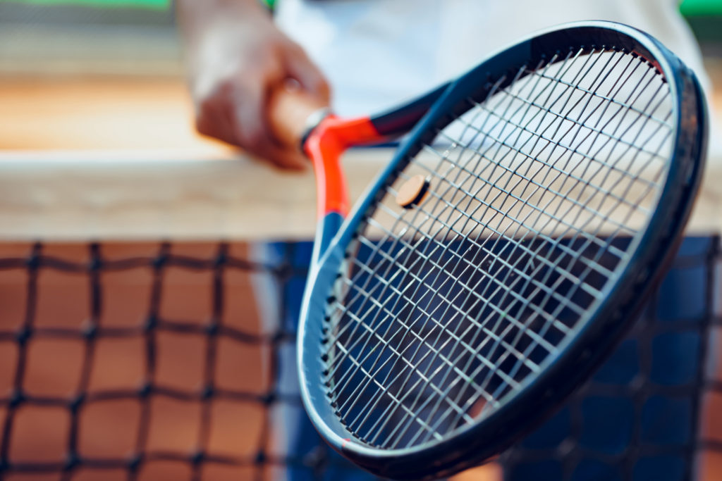 Close up of tennis racket resting on net with partial view of player in background